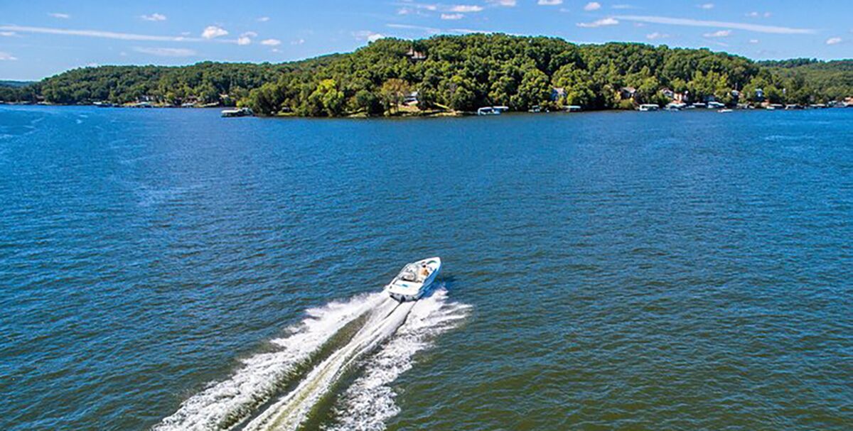 A boat sails on one of the most beautiful lakes in the US toward an islands of trees with residential docks scattered on the shore.