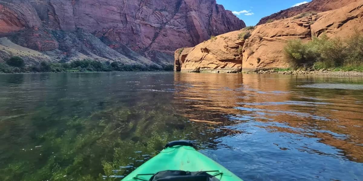 Kayaker paddling through canyon on calm river, one of the best places to kayak in the US for scenic views and peaceful water access.