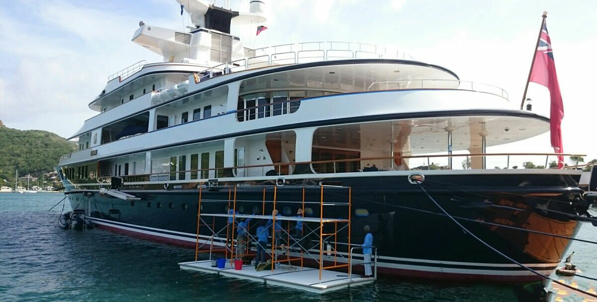 workers standing on a floating scaffolding platform repairing the side of a yacht