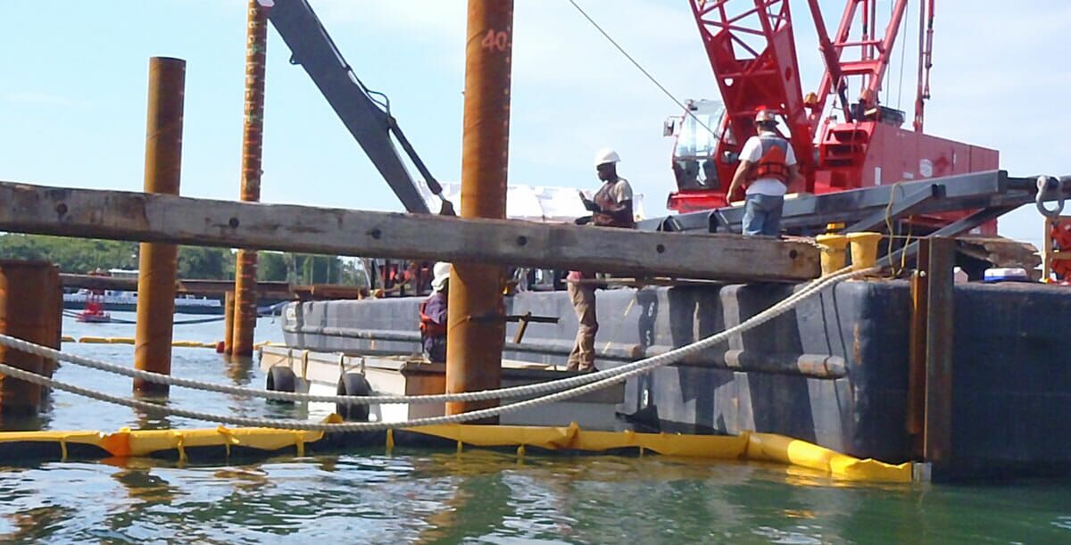 workers using a flat deck barge platform with heavy equipment flotation for a coastal construction project