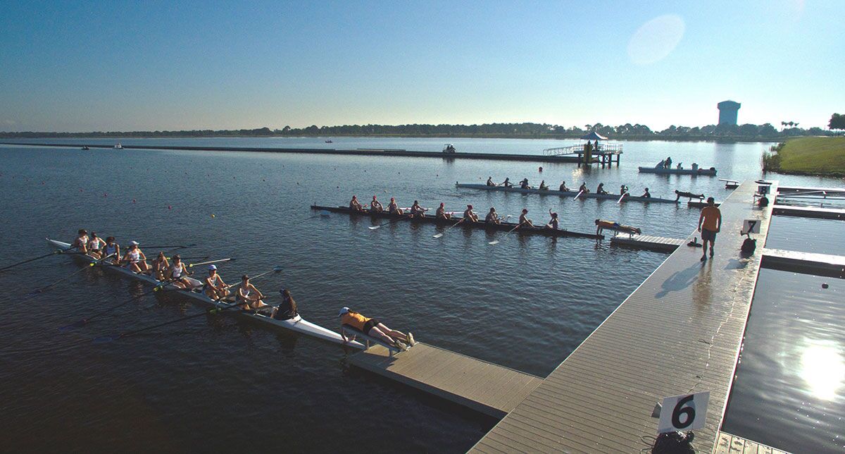 Several floating docks for college rowing facilities are being used by teams entering and exiting the water.