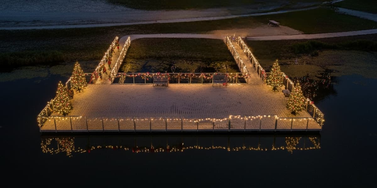 Floating dock decorated with Christmas trees and string lights at night for festive waterfront celebrations.