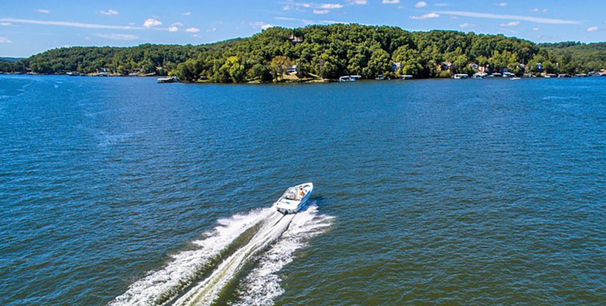 A boat sails on one of the most beautiful lakes in the US toward an islands of trees with residential docks scattered on the shore.