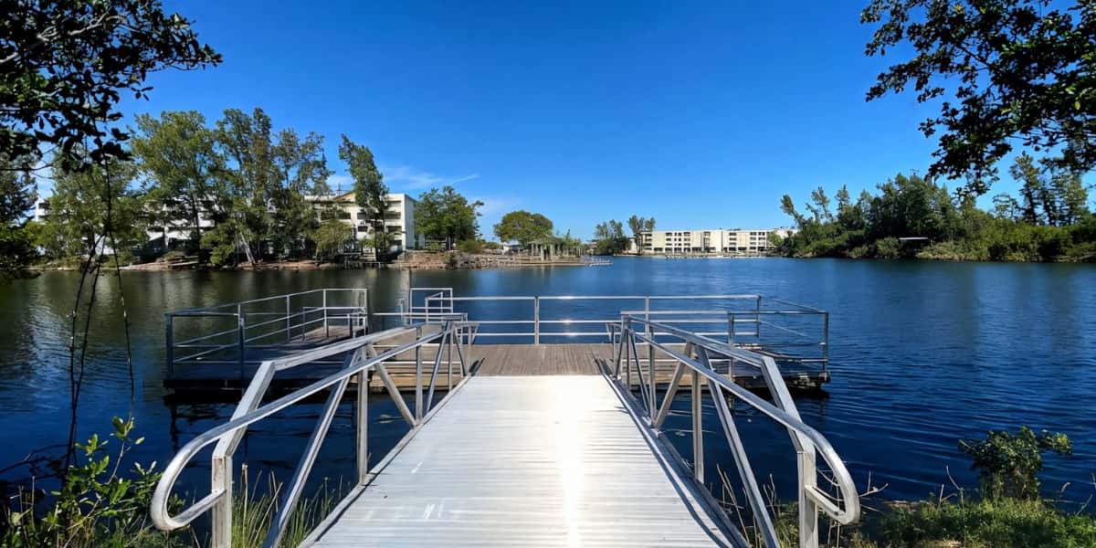 Wooden pier with metal railings extending into a blue lake, surrounded by trees and residential buildings, providing an ideal location for pier fishing tips and techniques.